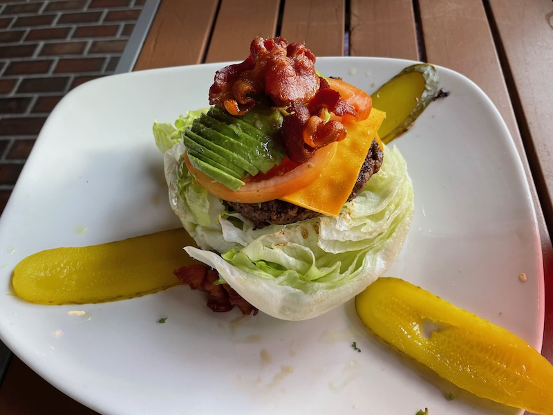 Lettuce-wrapped burger with bacon, avocado, and cheese on white plate